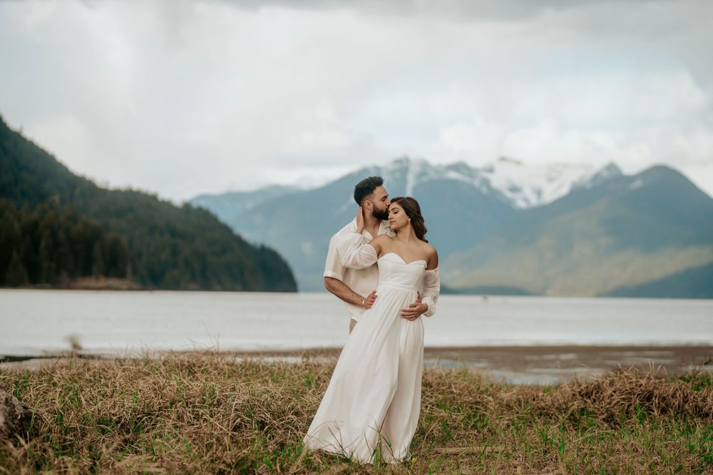 A romantic mountain elopement photo with a couple embracing against a backdrop of snow-capped peaks and a lake.