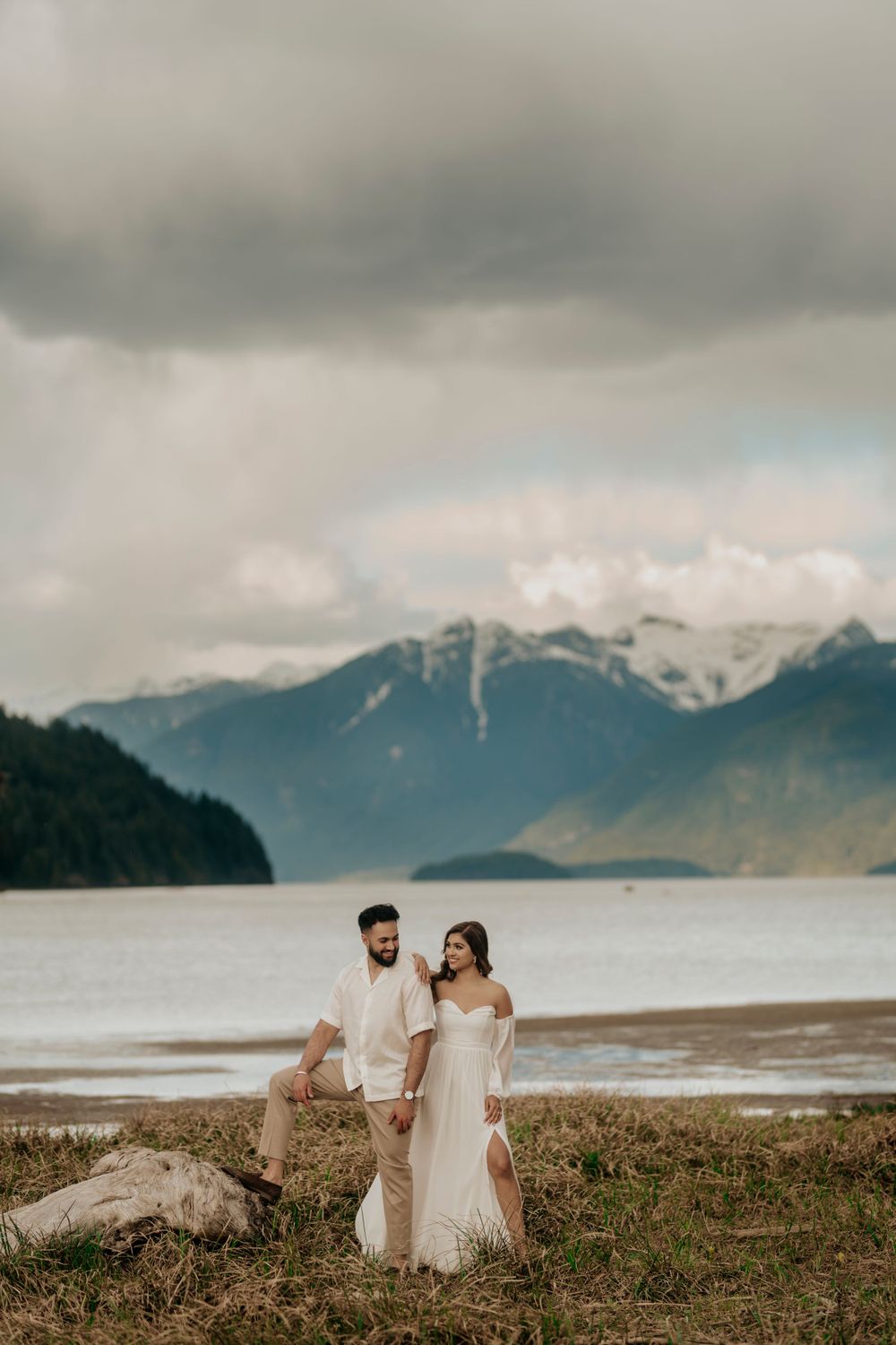 An intimate wedding portrait with a couple standing on a hillside overlooking dramatic mountain ranges and waterfront.