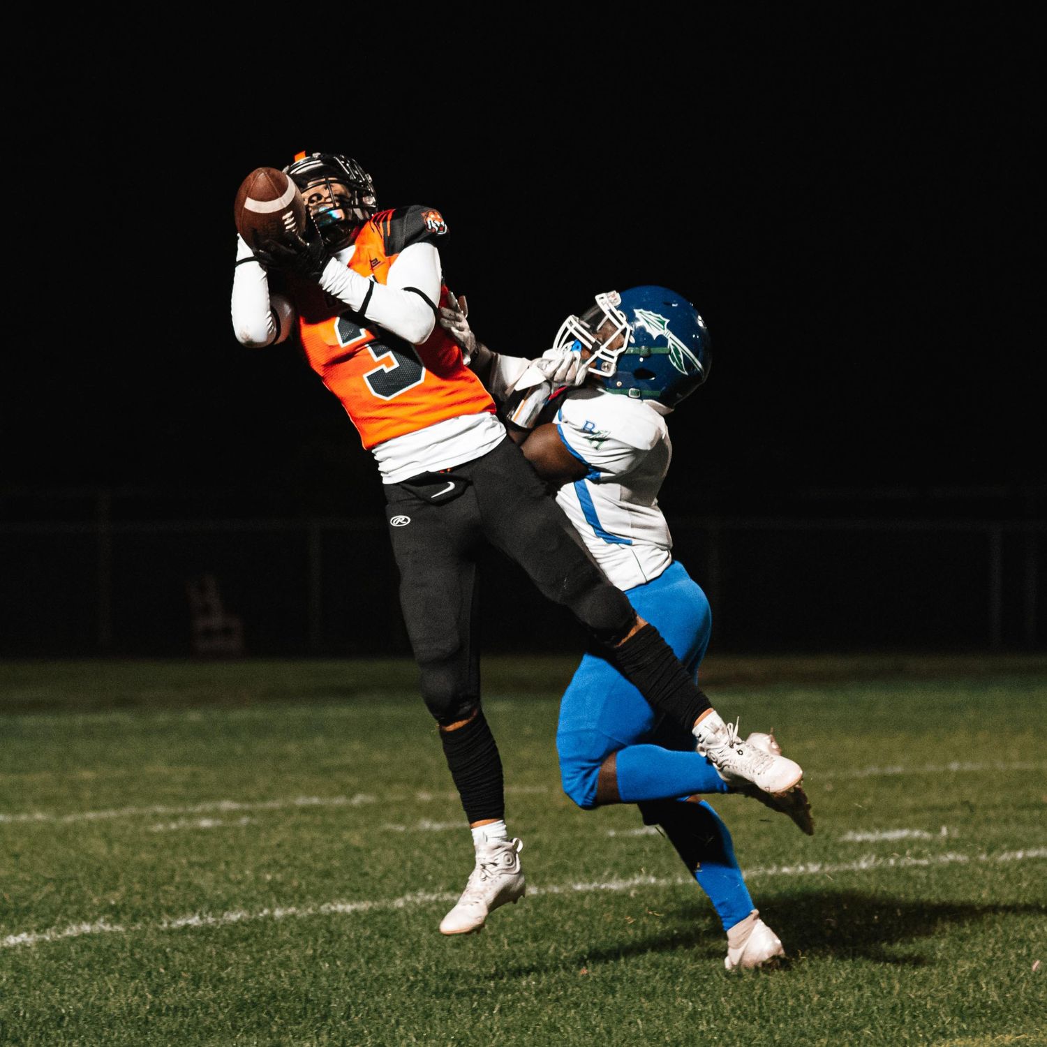Football player in orange jersey leaping to catch pass while defender attempts to block.