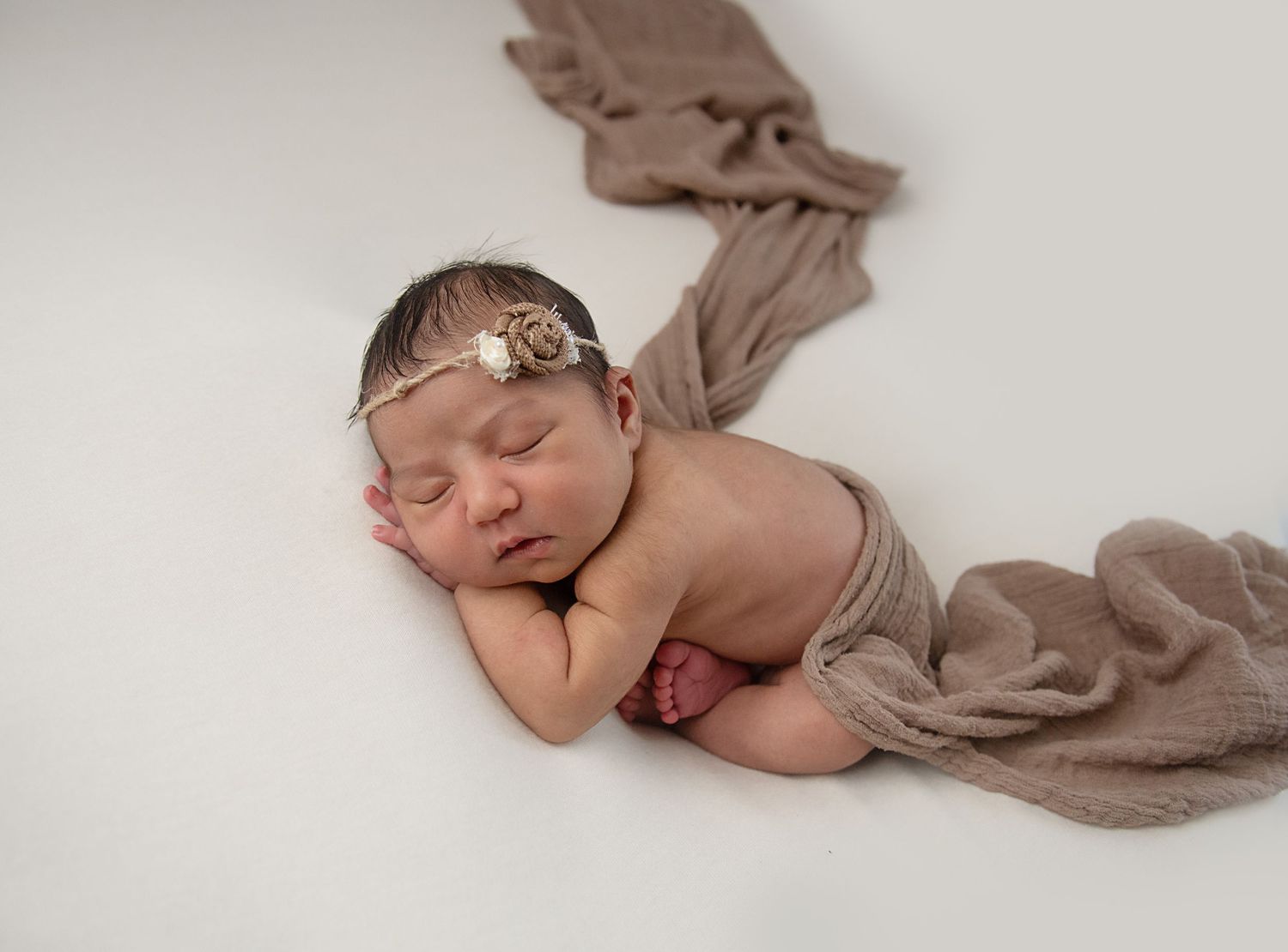 Sleeping newborn baby posed with brown fabric in minimalist studio setting.