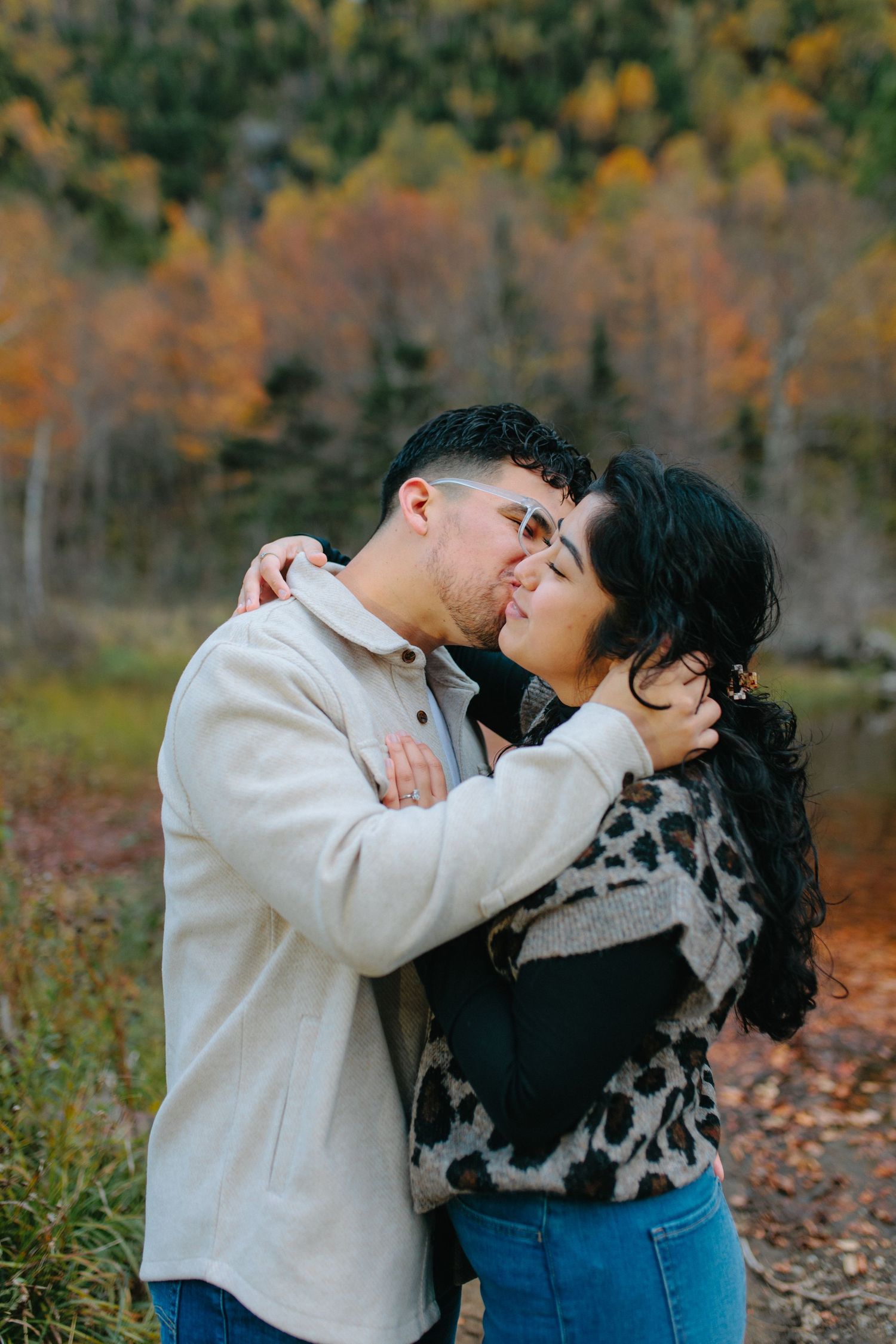 A couple shares a tender embrace while standing outdoors among autumn foliage in a romantic photoshoot sequence.