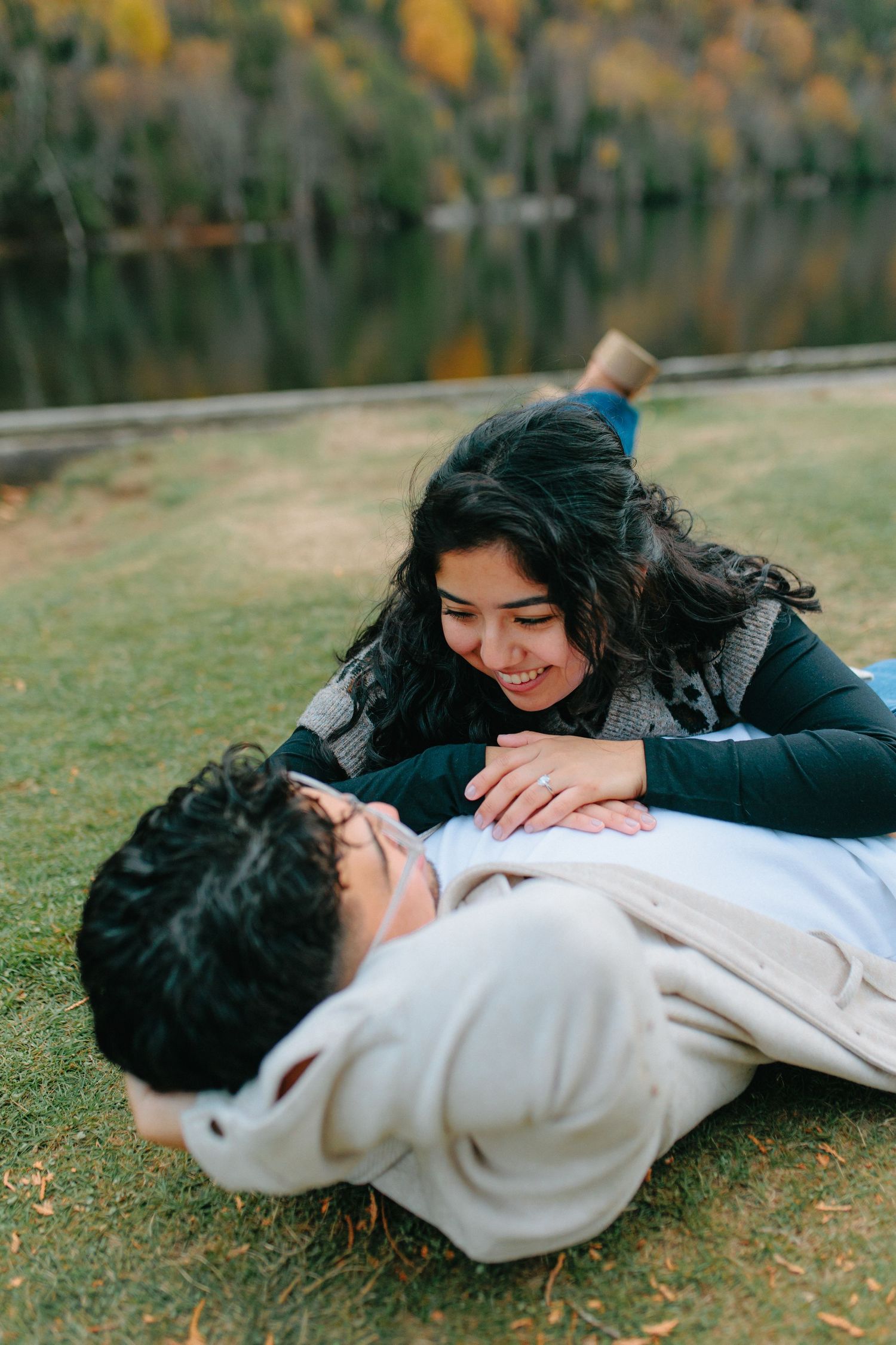 A couple lies on autumn leaves during an intimate outdoor photo session near a mountain lake.