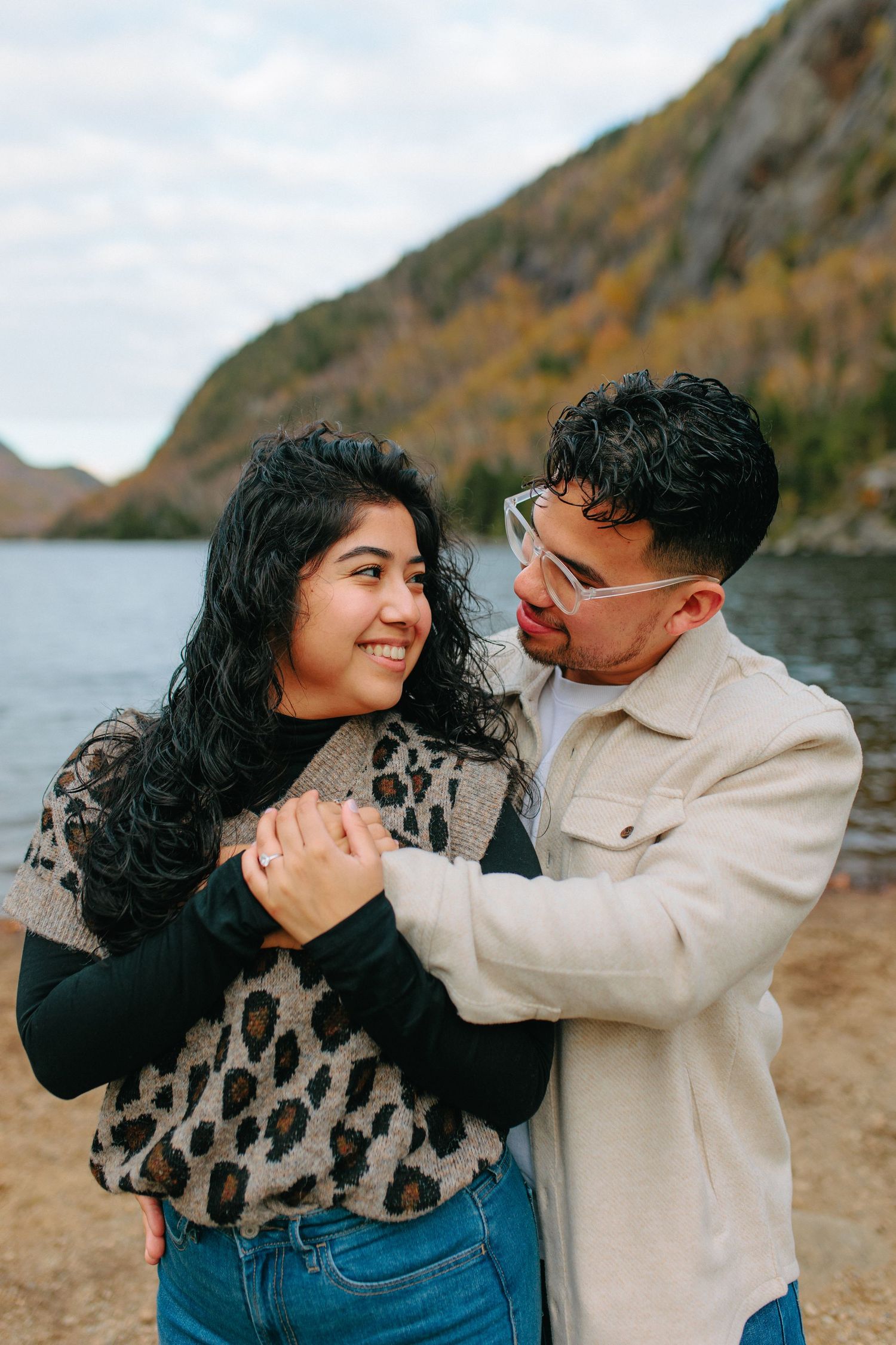 A couple shares joyful moments by a scenic lake surrounded by fall foliage on mountain slopes.