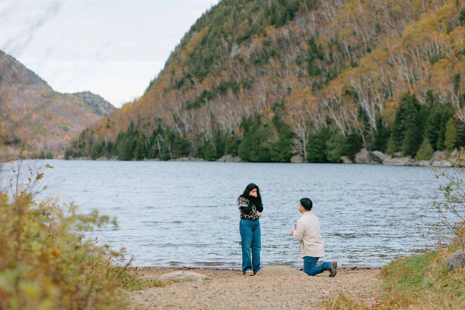 Scenic autumn landscape with people enjoying views of a lake surrounded by colorful fall foliage in the mountains.