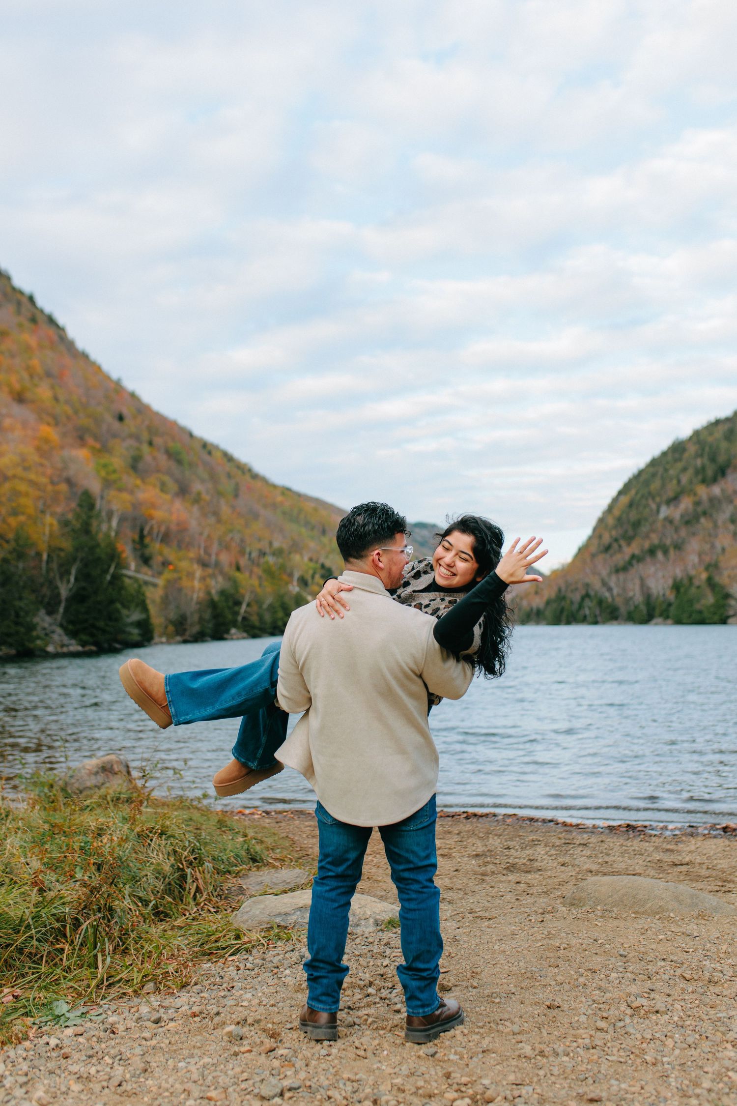 A playful couple enjoying a romantic moment by a lake surrounded by autumn mountains and colorful fall foliage.