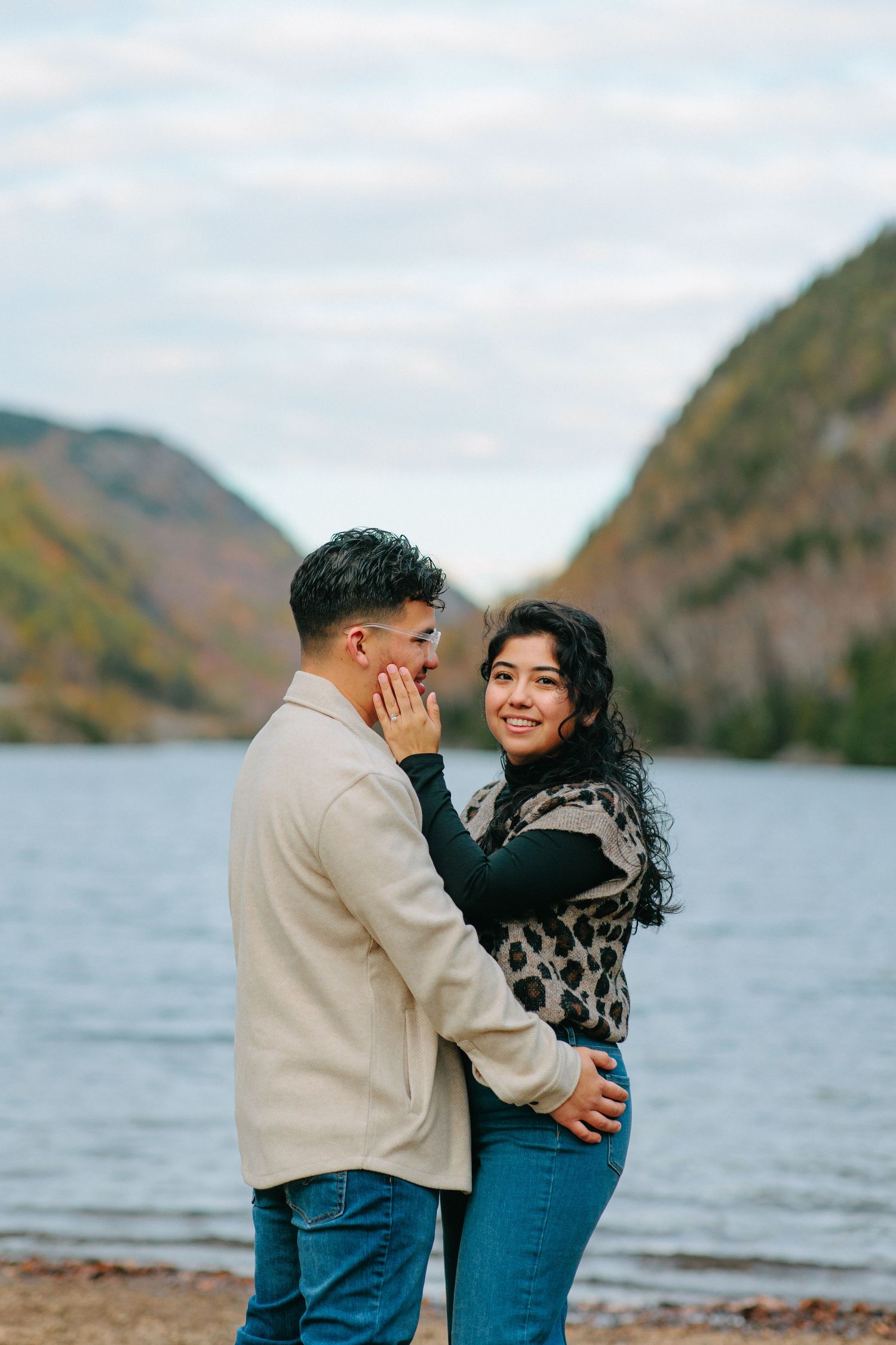 A couple shares romantic moments by a scenic mountain lake on a cloudy autumn day.