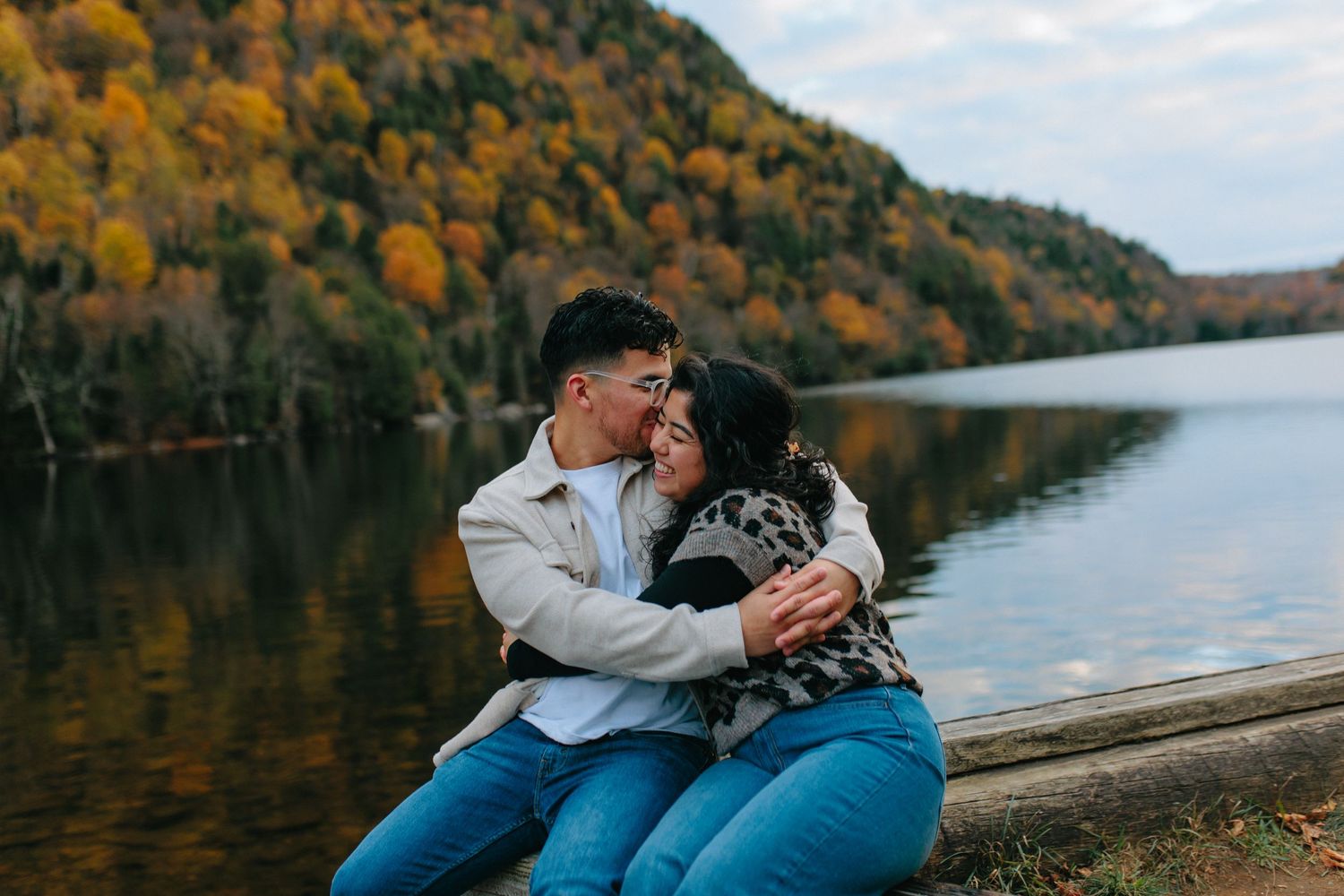 Couple sharing romantic moments by a serene autumn lake surrounded by colorful fall foliage.