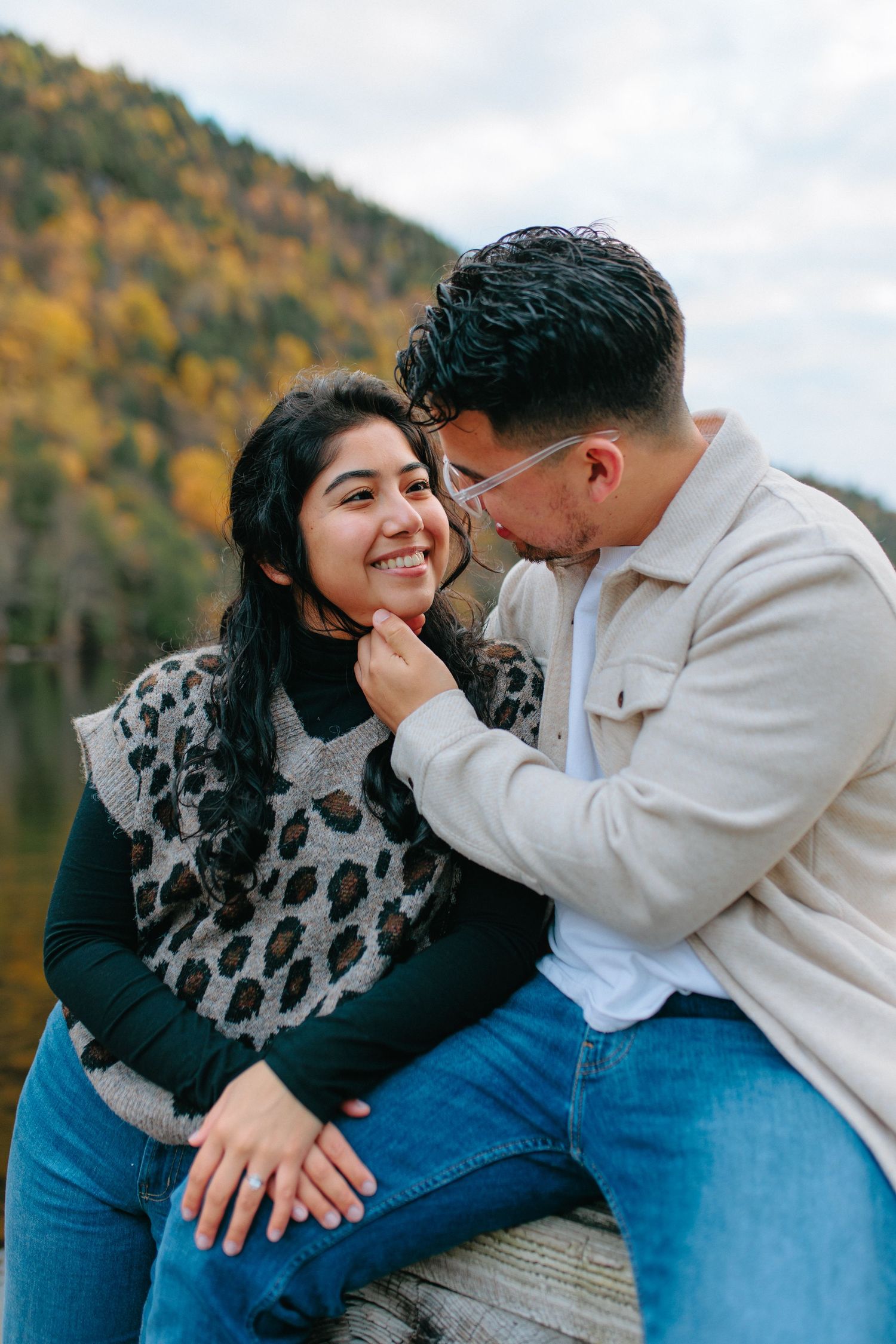 Romantic couple sharing intimate moments on a dock with autumn foliage in the background.