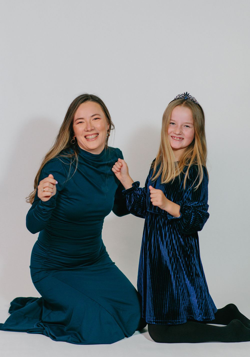 Two friends in dark blue outfits sitting and laughing together in a photo collage against a light background.