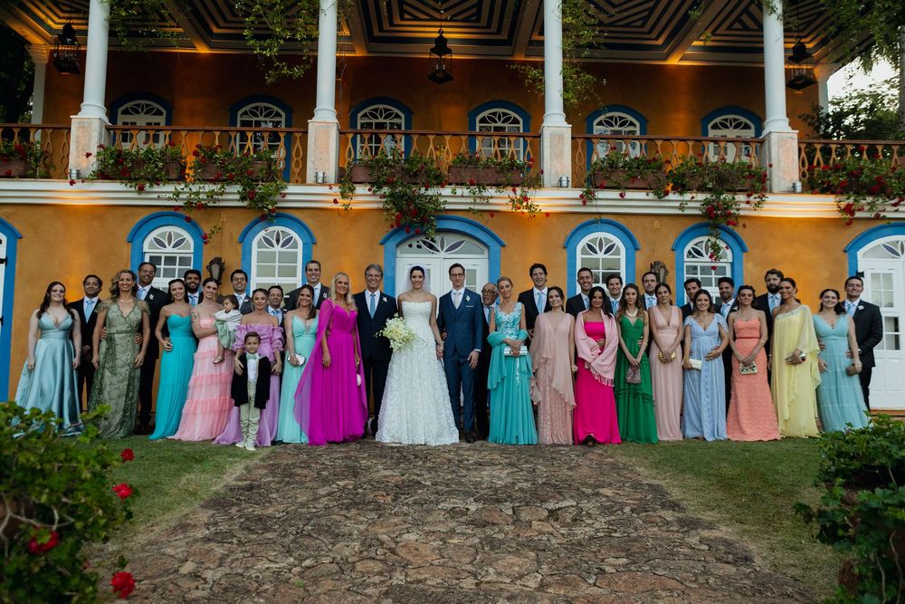 Wedding party members in colorful formal attire stand in a line against a yellow building exterior.