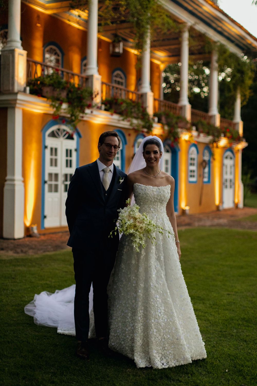 A couple in formal wedding attire walks together outside a historic columned building at dusk.