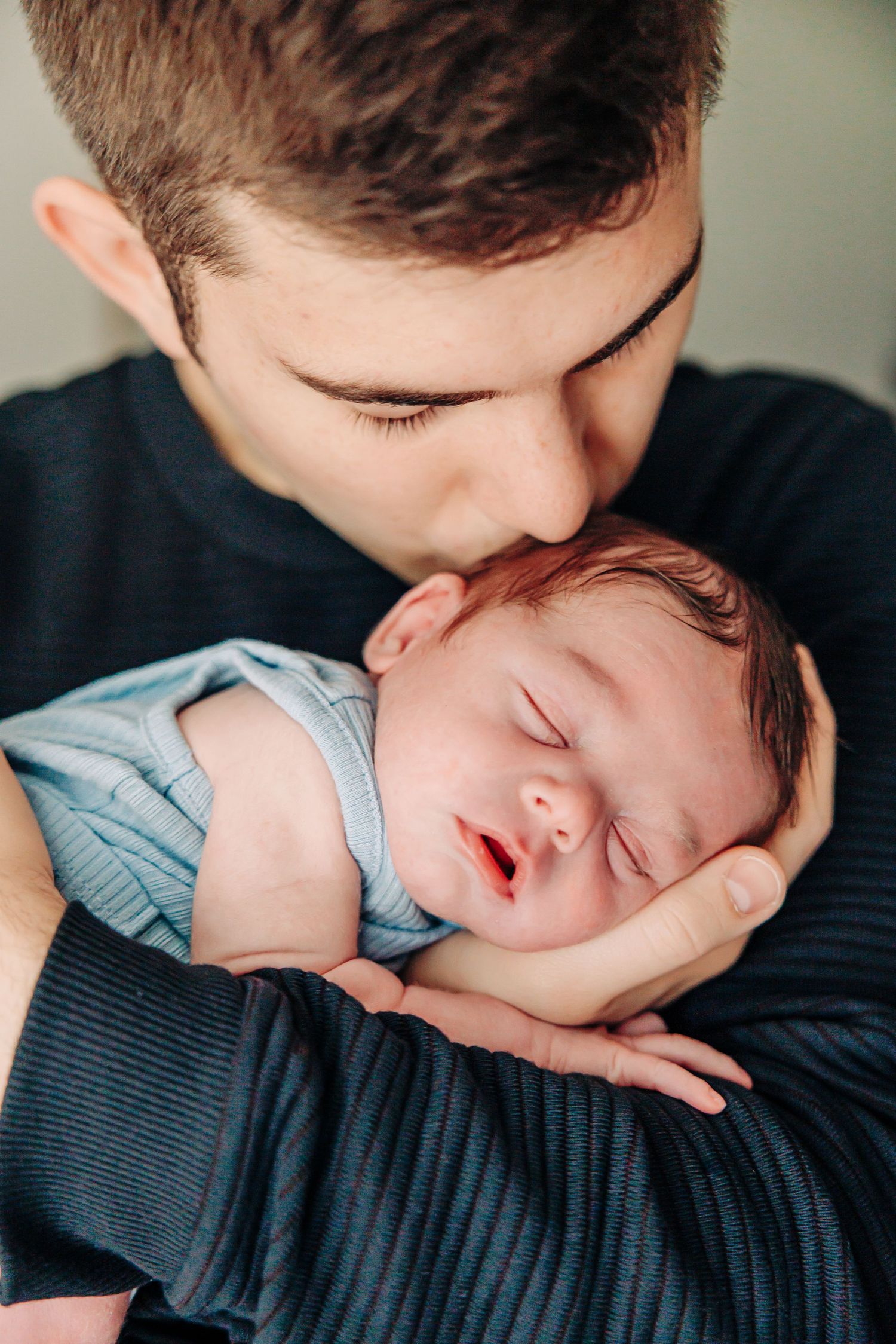 A sleeping baby in a light blue shirt rests peacefully against a dark textured fabric background.