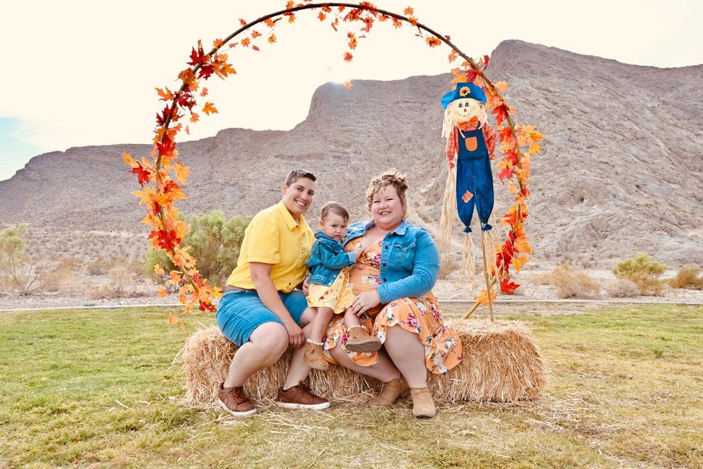 A family in yellow and blue outfits poses on hay bales under a fall leaf arch.