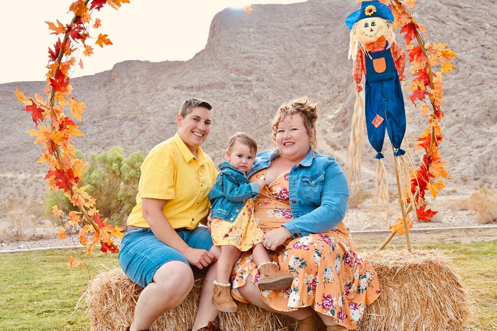 A family of three in colorful outfits poses on hay bales under a fall arch.