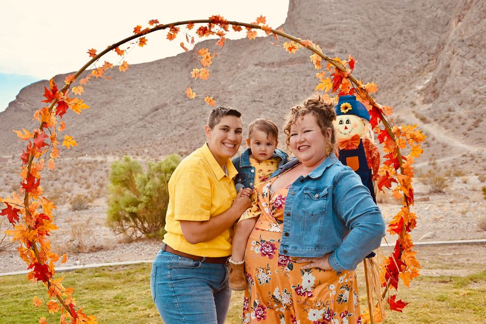 Happy family smiling together under a circular fall foliage arch with scarecrow in background.