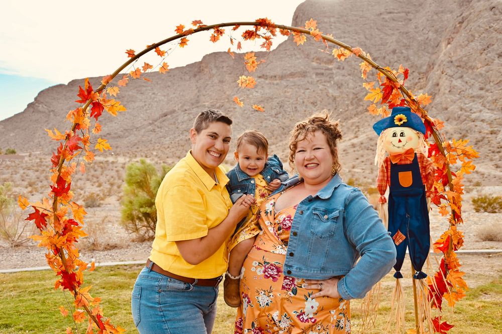 Joyful family posing under circular fall leaf arch with scarecrow decoration in outdoor setting.