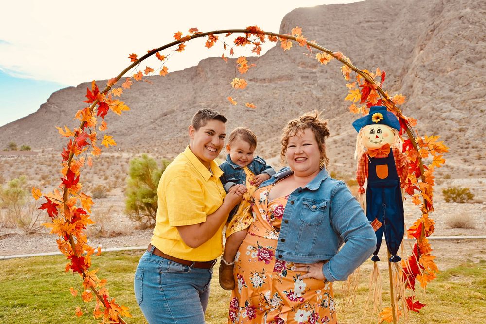 Happy family portrait under colorful fall arch with scarecrow decoration in desert landscape.