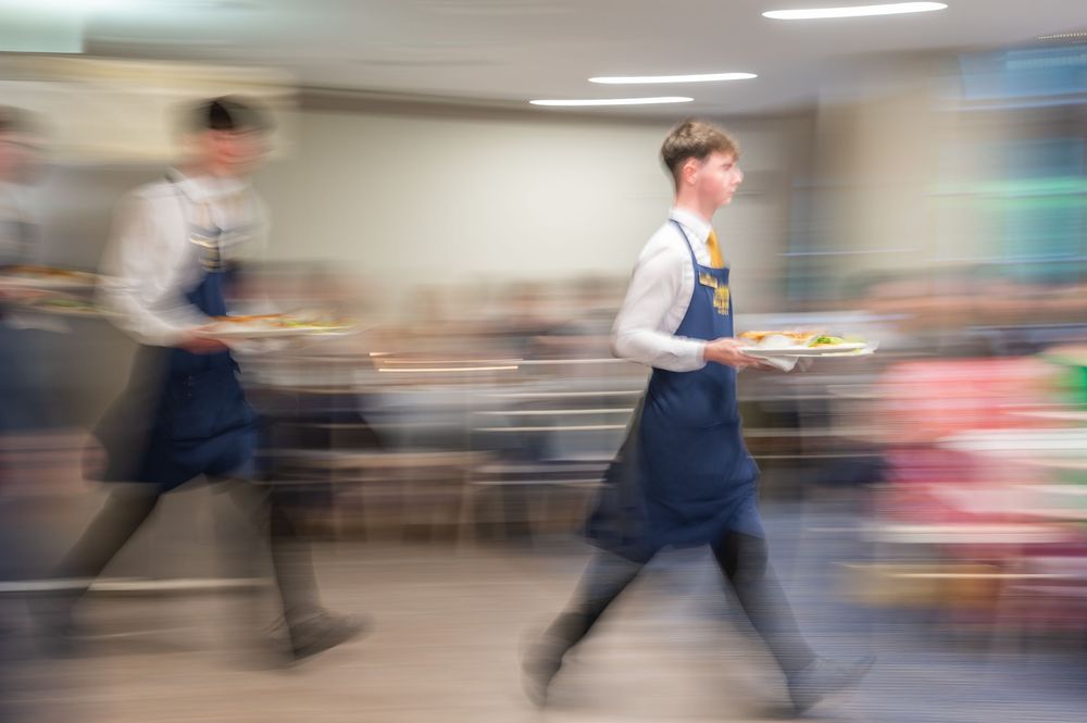 Motion-blurred scene of waiters walking through an elegant indoor venue during a formal event.