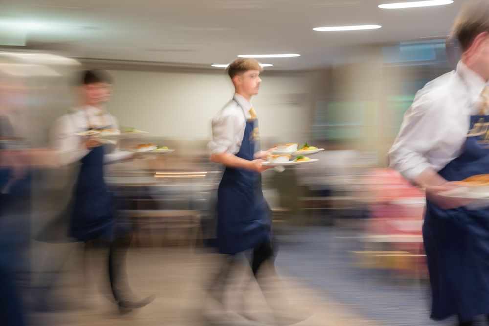 Motion-blurred scene of waiters walking through an elegant indoor venue during a formal event.