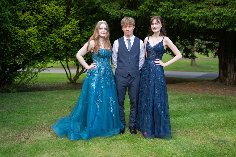 People in formal attire posing outdoors against a lush green garden backdrop.