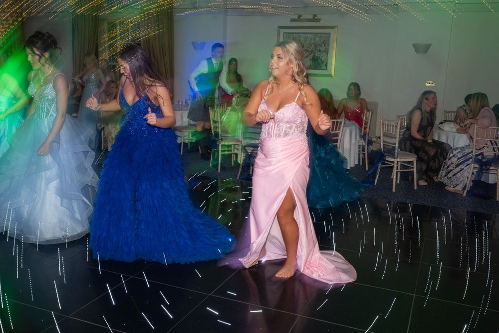 Colorful dance party scene with green lighting and formal dresses in motion.