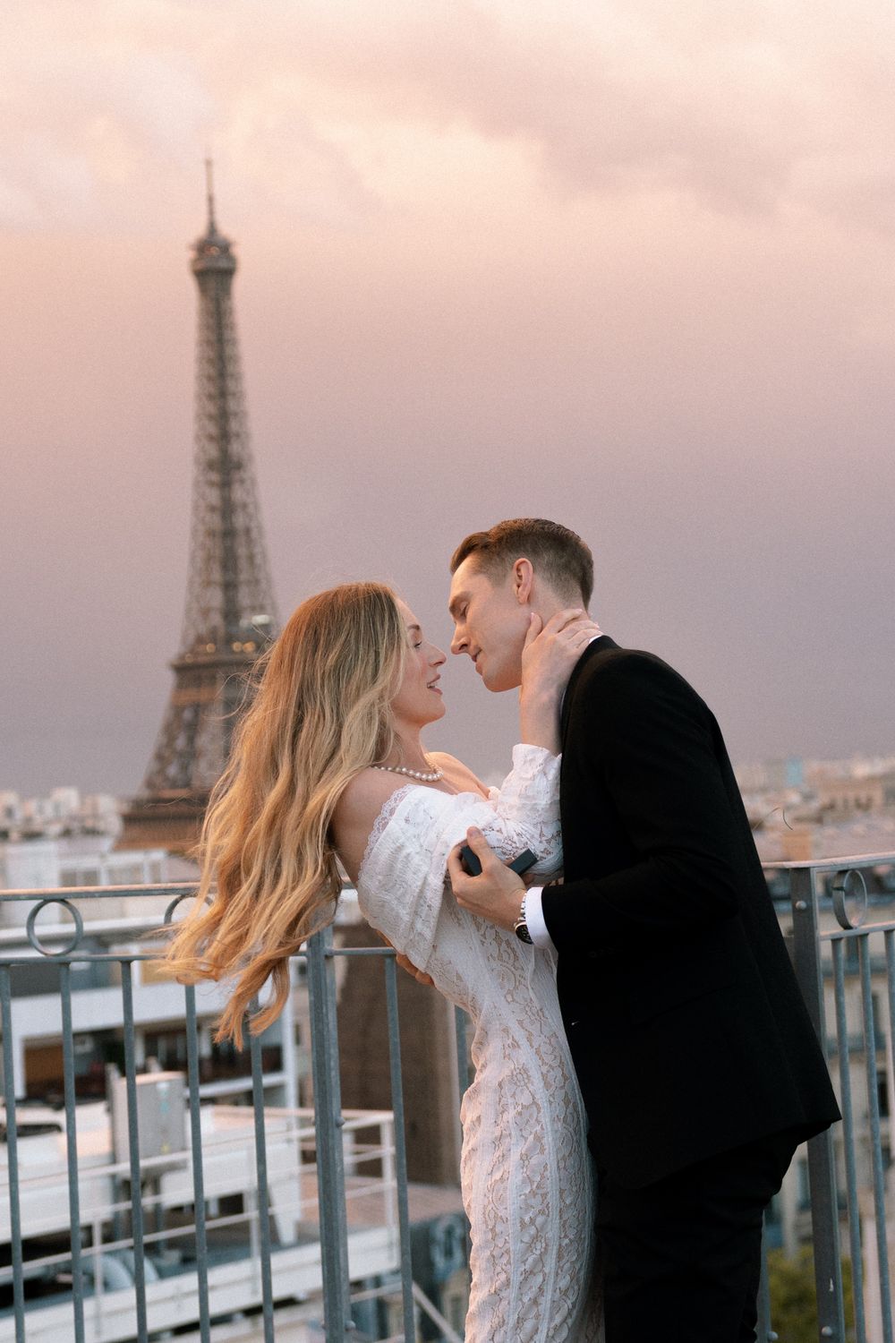 A romantic couple shares intimate moments on a Paris rooftop terrace with the Eiffel Tower visible in the background.