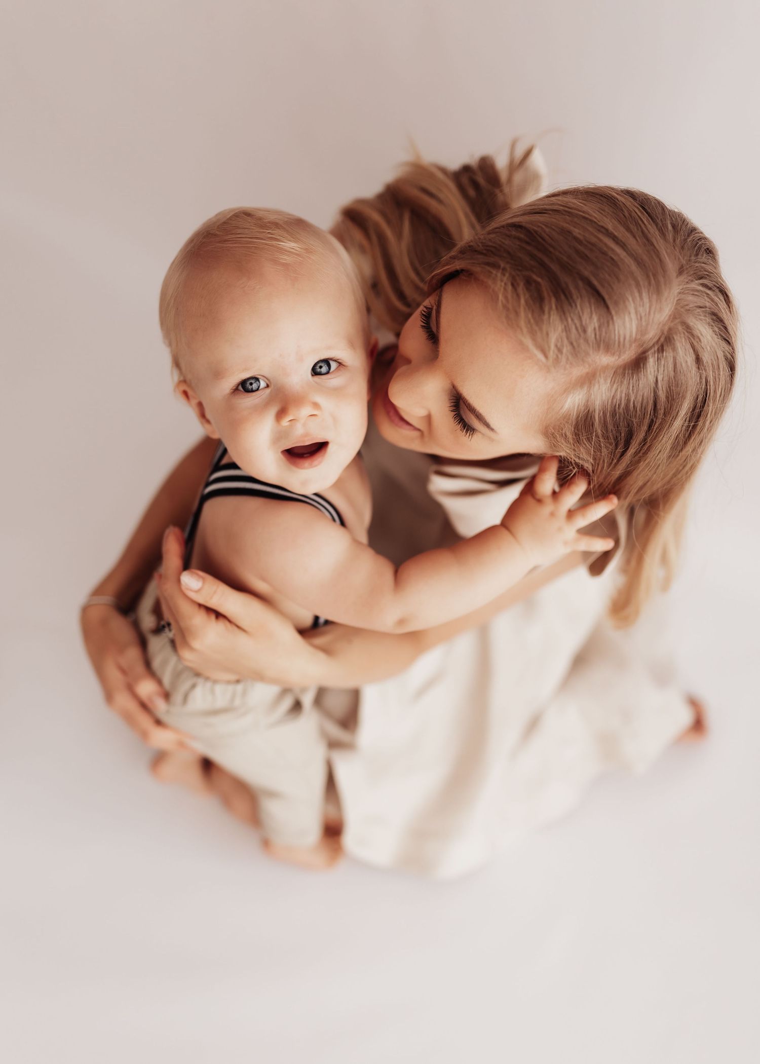A tender moment captured from above showing a parent and baby in white clothing against a neutral background.