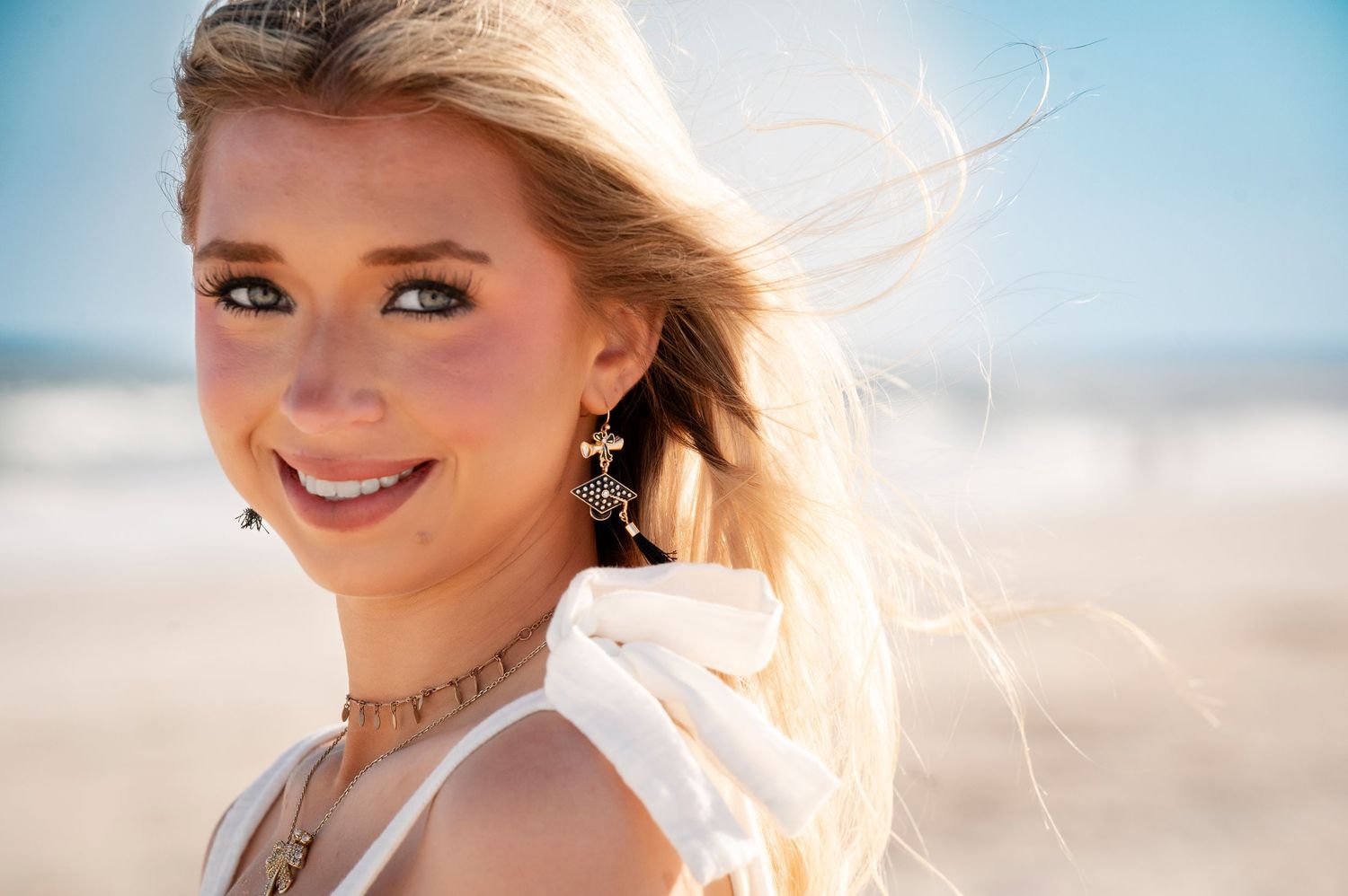 A person in a white dress walks along the shoreline as waves gently roll onto a sandy beach at sunset.