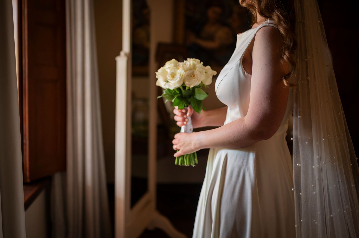 Wedding party members in white dresses hold bouquets while standing in an elegant indoor venue.