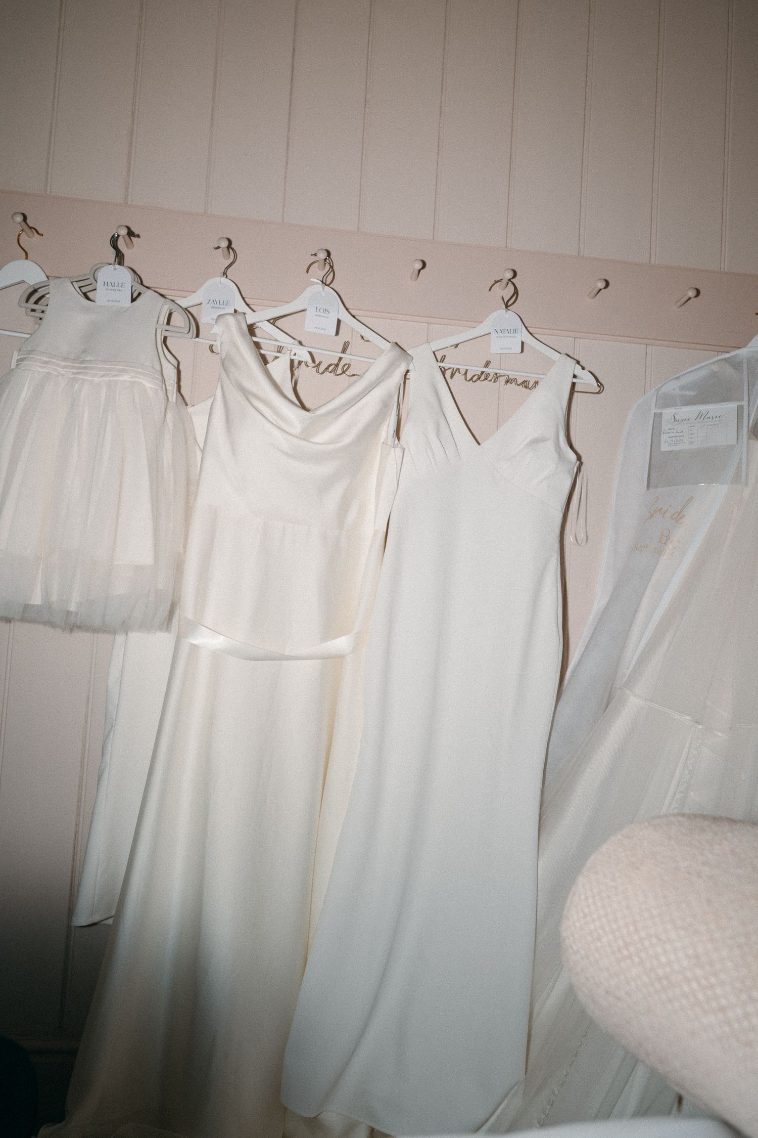 White sleeveless garments hanging on a clothing rack against a pale wall in soft lighting.