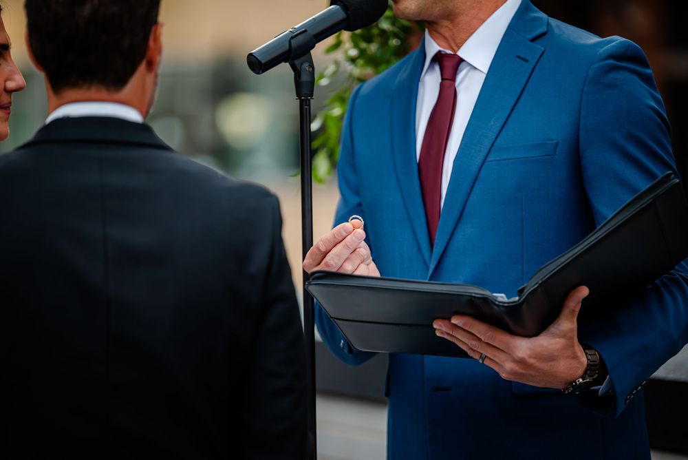 Professional in a navy suit and red tie holds a black folder while standing in a business setting.