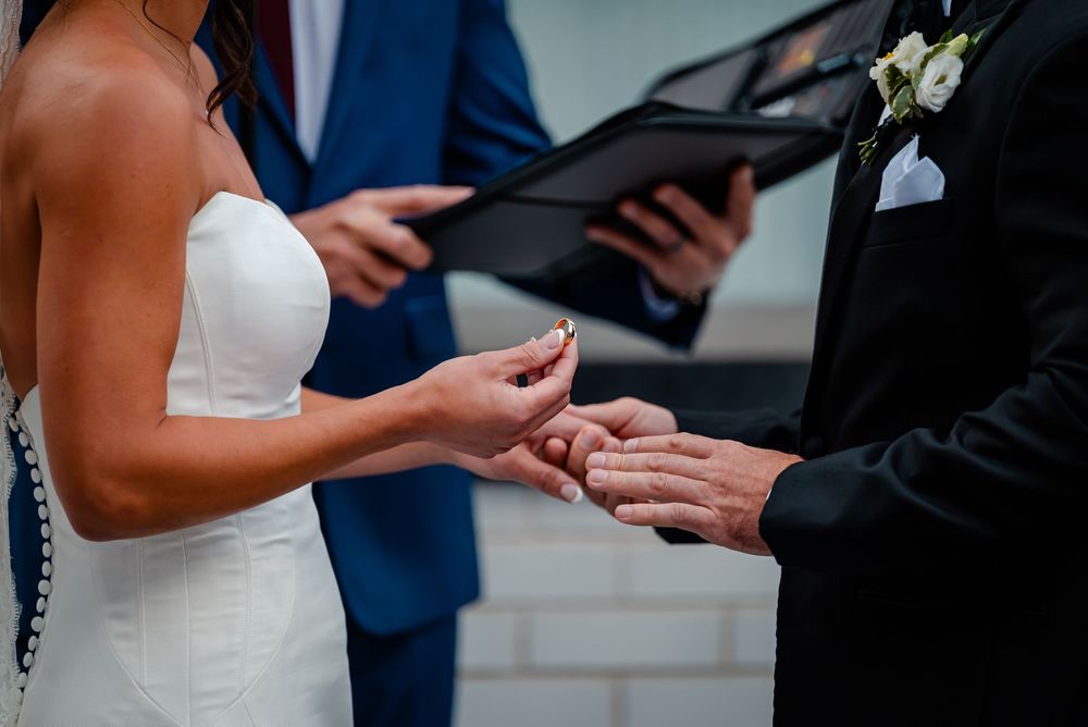 Close up of hands exchanging wedding rings during an elegant ceremony with a navy suit and white dress.