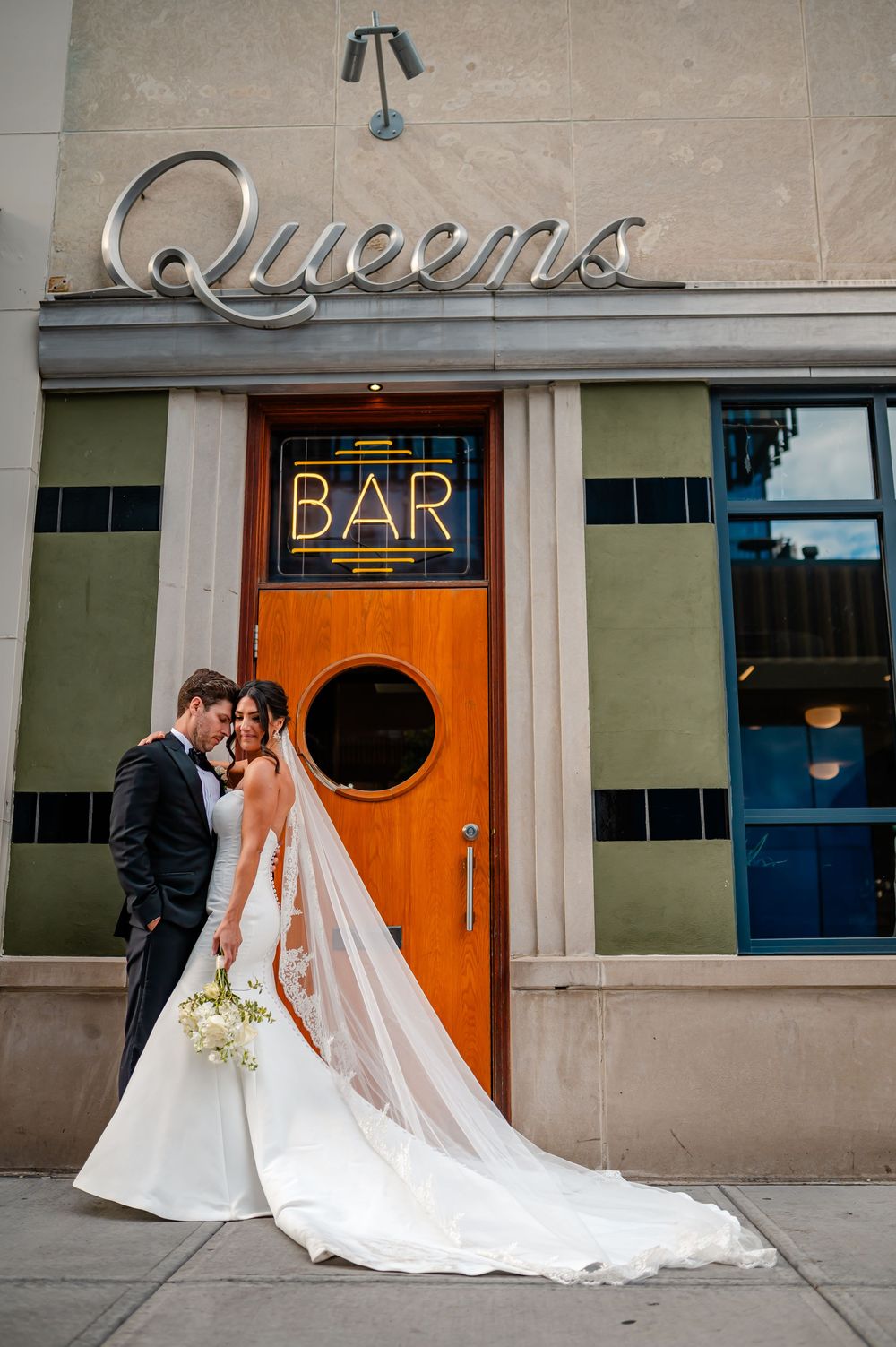 A wedding couple poses in front of orange doors and art deco signage at a historic venue.