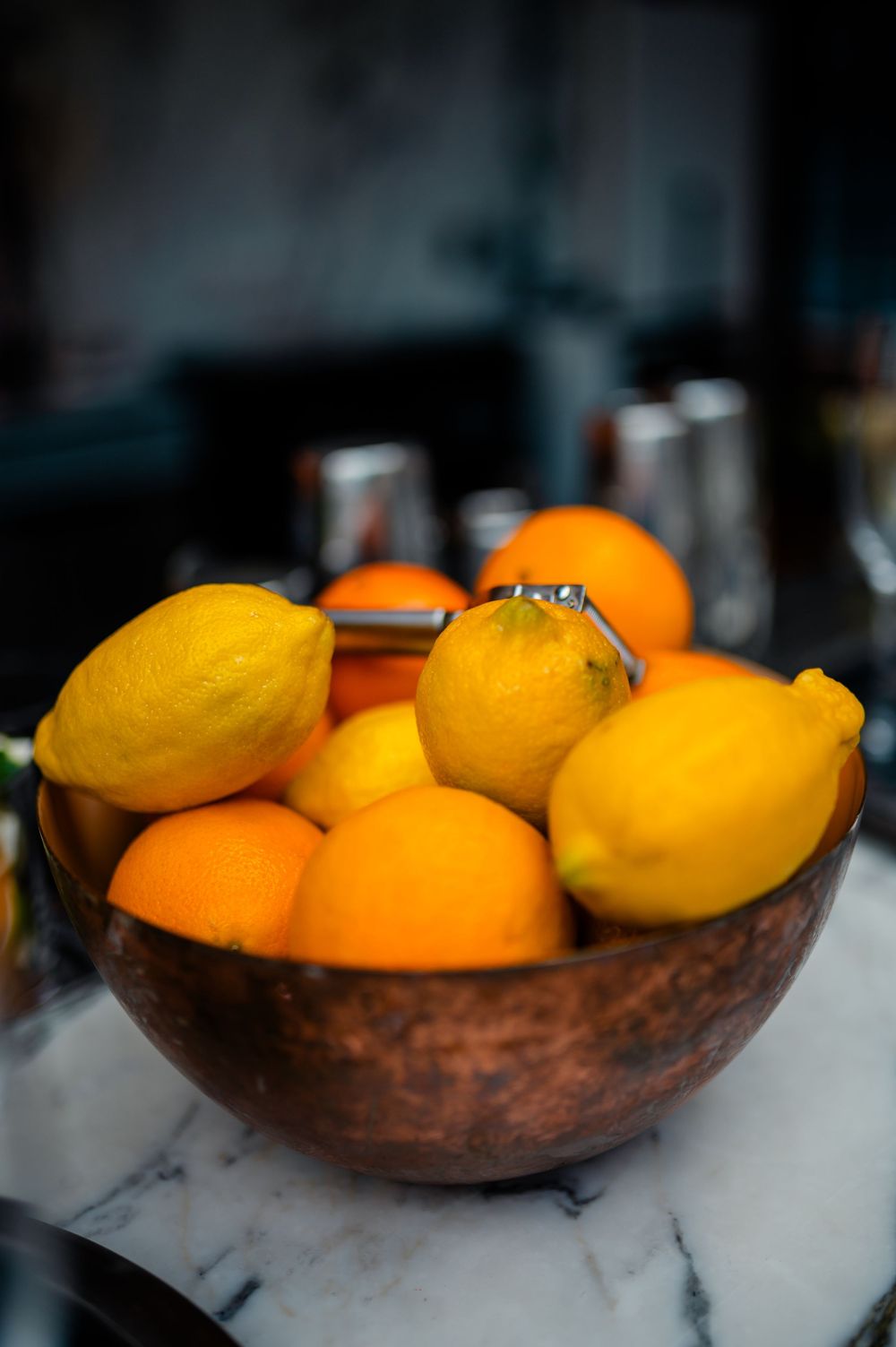 Fresh citrus fruits including oranges and lemons arranged in a rustic wooden bowl on a marble surface.