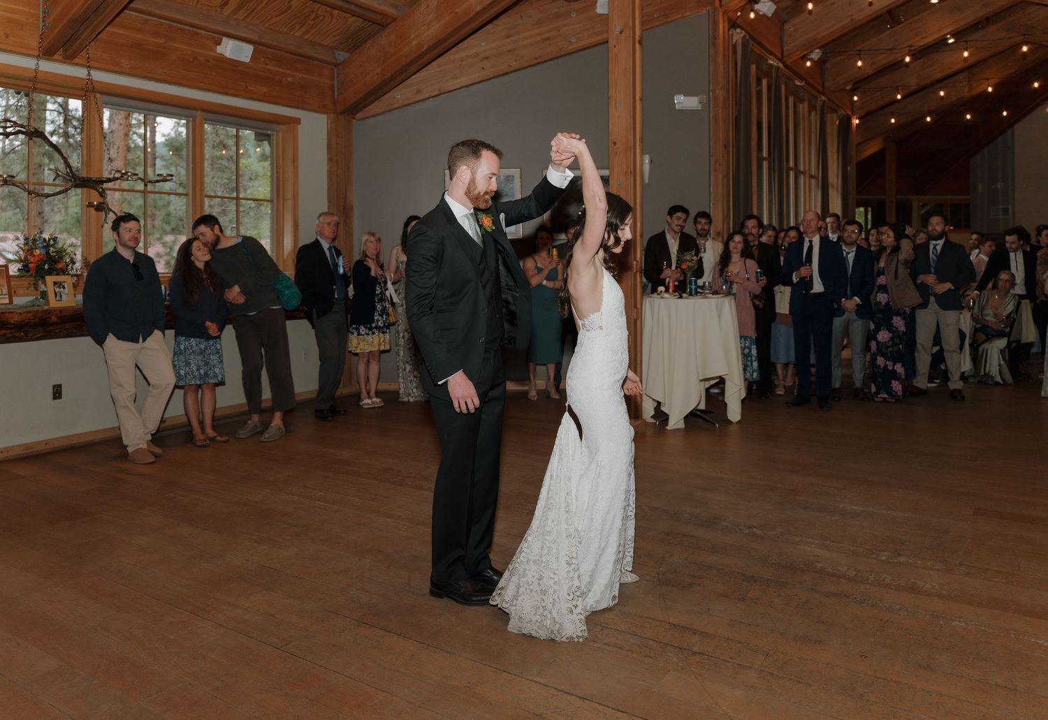 Wedding reception dance scene in a rustic wooden barn venue with string lights overhead.
