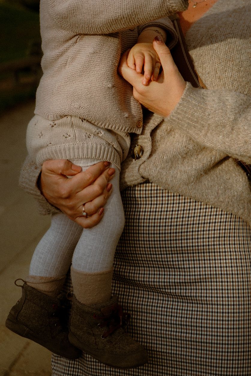 Close-up of tiny feet in knit booties being held by gentle hands in cozy winter clothing.
