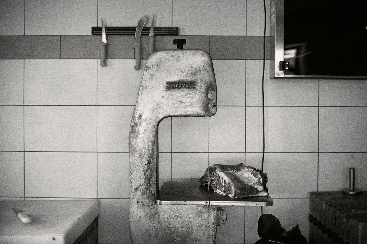 Black and white photograph of a tiled wall with a mounted TV screen visible in the corner.