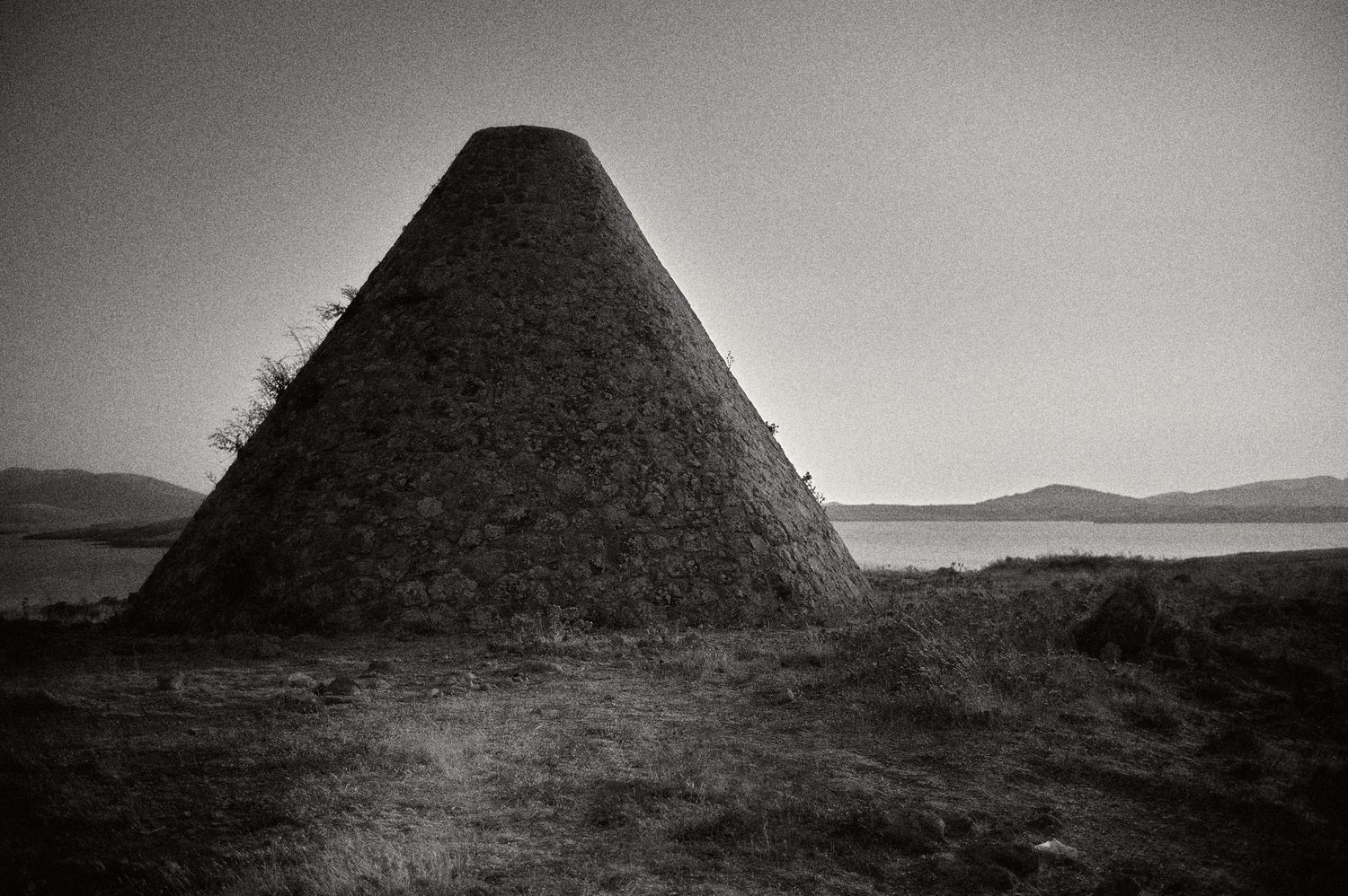 Ancient stone pyramids stand silhouetted against a moody sky in a stark desert landscape.