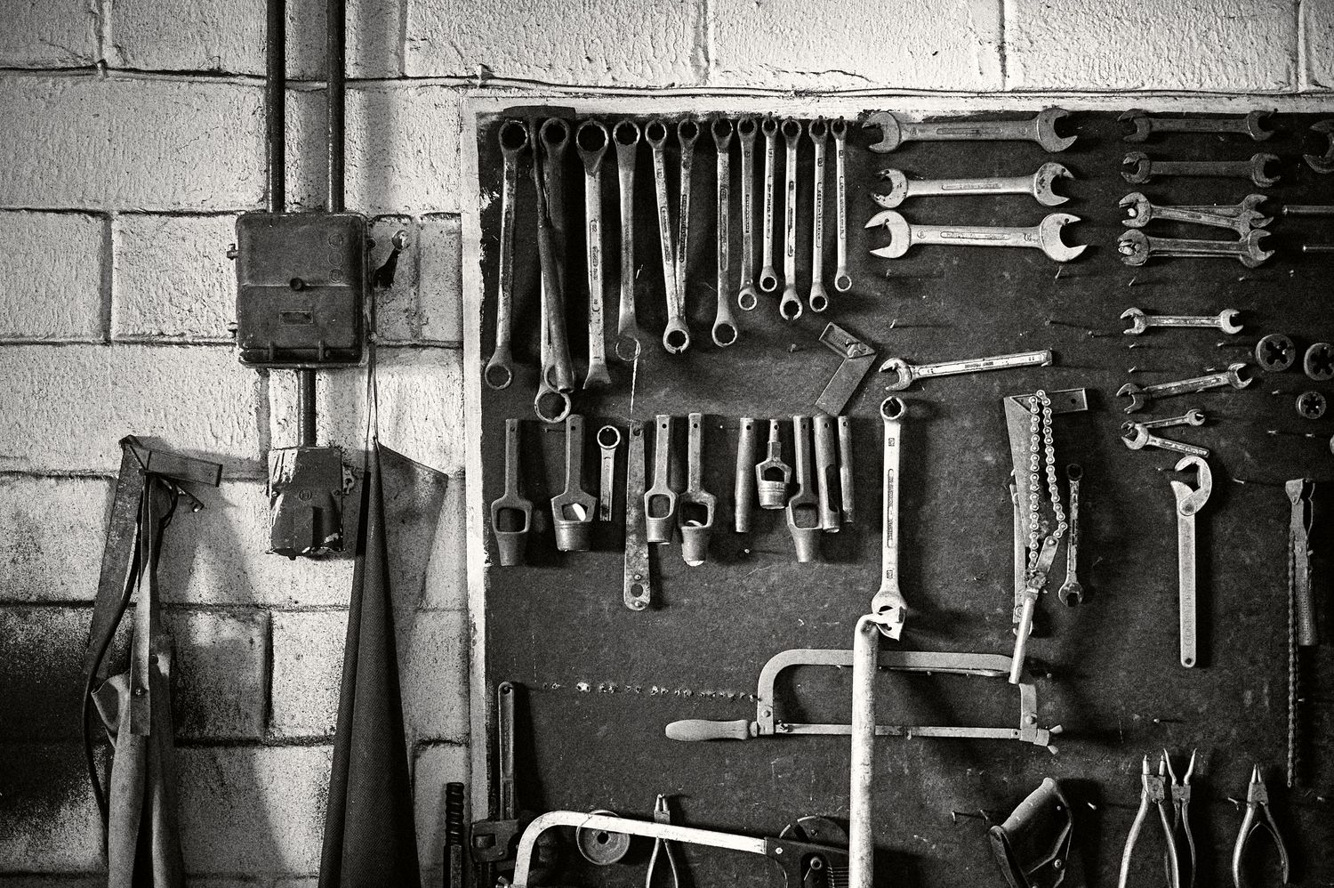 Vintage workshop interior with tools hanging on wall and workbench displaying various mechanical equipment and supplies.