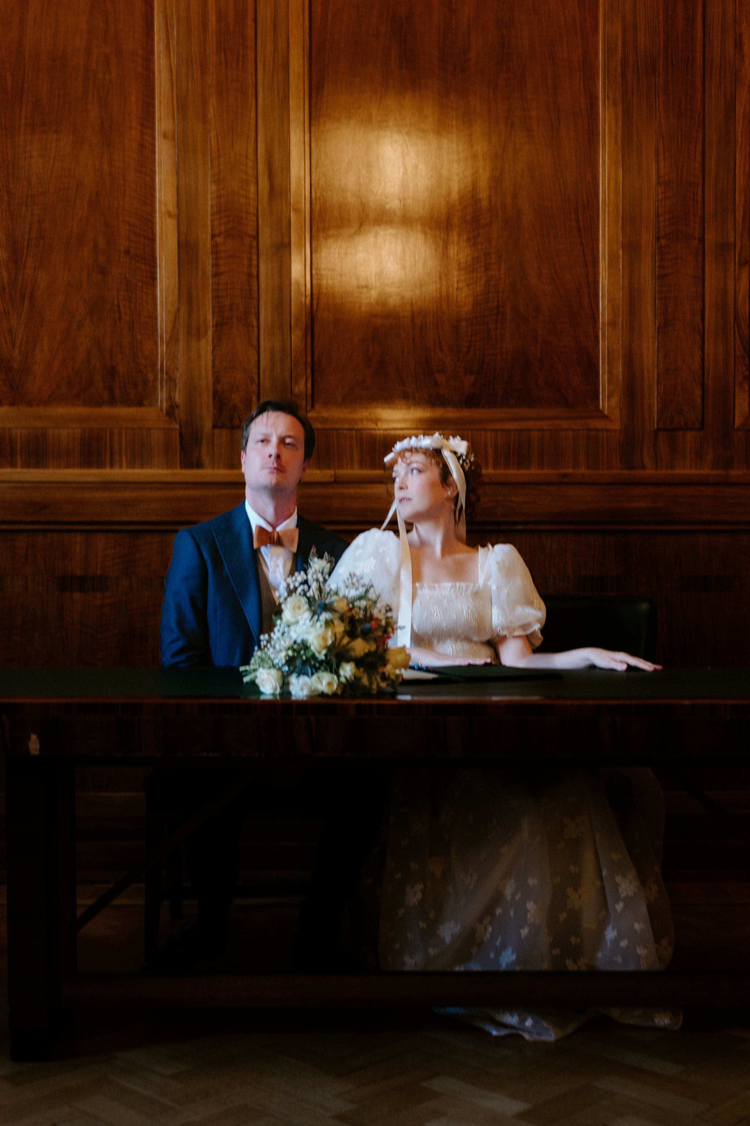 A sequence of four wedding photos showing a couple signing documents in a dark wood-paneled room with dramatic lighting.
