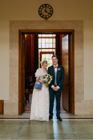 A wedding couple poses in a series of elegant hallway shots with marble walls and wooden doors.
