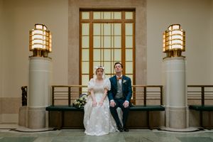 A bride and groom share a tender moment in an elegant stone colonnade with Mission-style wall sconces.