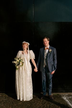 A couple in wedding attire stands against a dark wall in a series of artistic wedding photos.