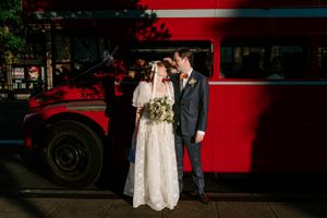 A wedding couple poses near a vintage red double-decker bus during their photo session.