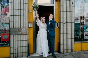 A couple in wedding attire poses in front of an urban wall with posters and graffiti for artistic wedding photos.
