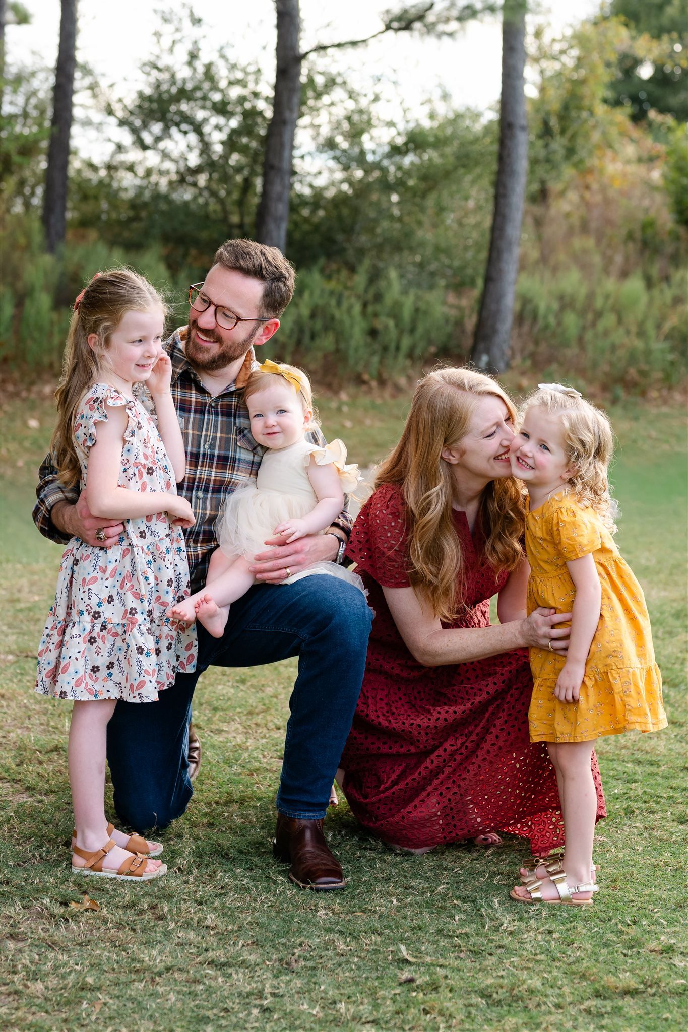 A loving family sits together on grass during an outdoor autumn photoshoot wearing coordinated red and floral outfits.
