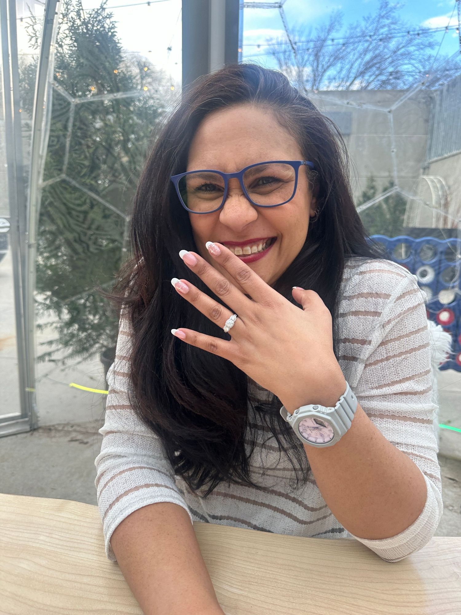 A person in glasses and dark hair laughs while covering their mouth with their hand at a table.