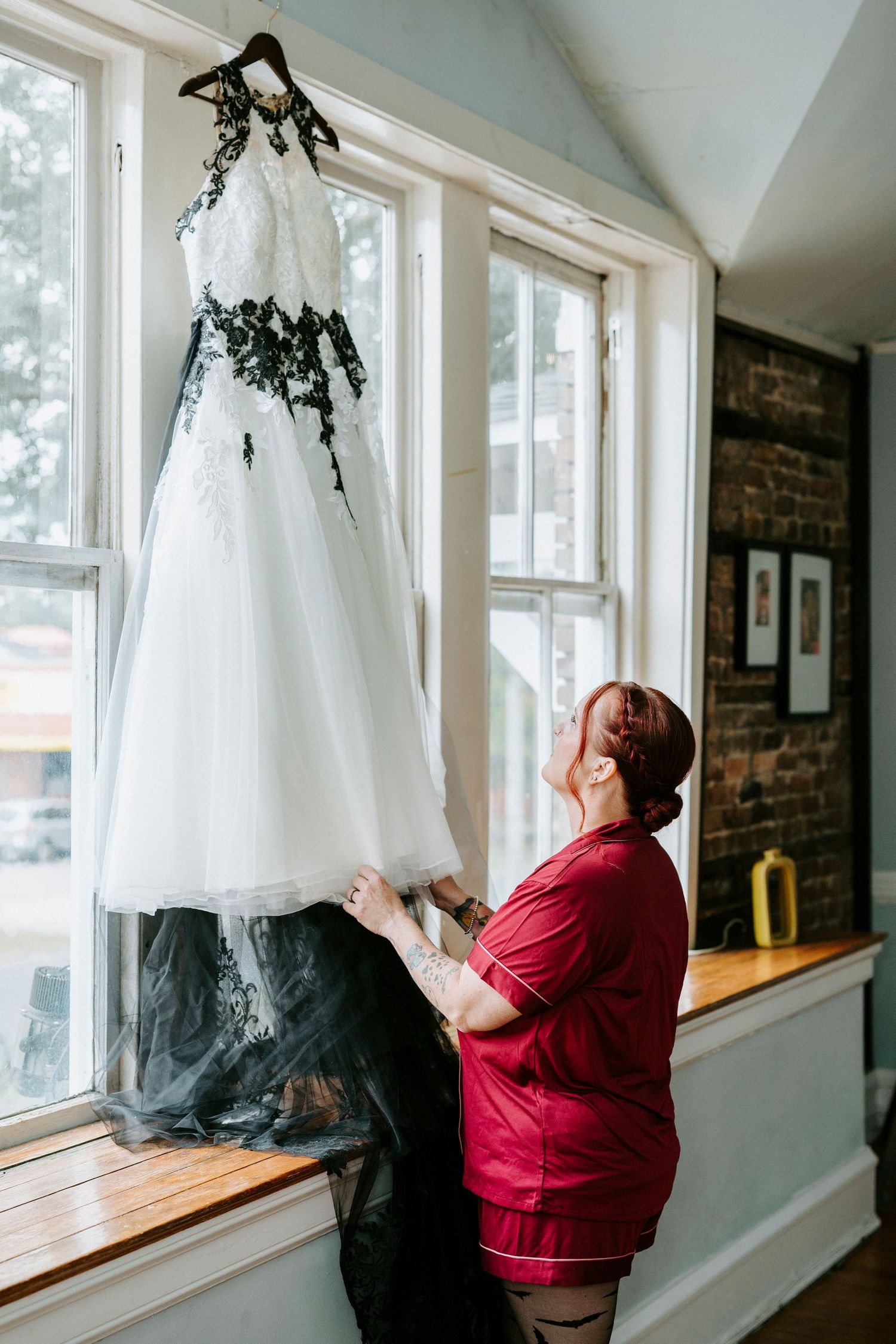 Person in red shirt hangs up white dresses with black bottoms in a bright room with windows.