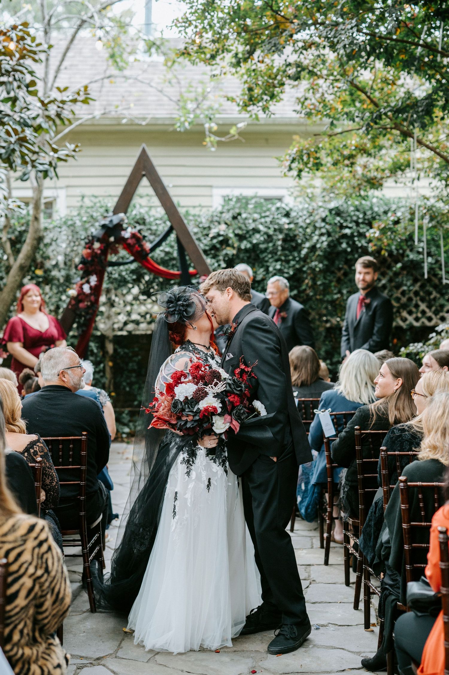 Wedding ceremony guests stand and celebrate as newlyweds walk down the aisle at an outdoor garden venue.