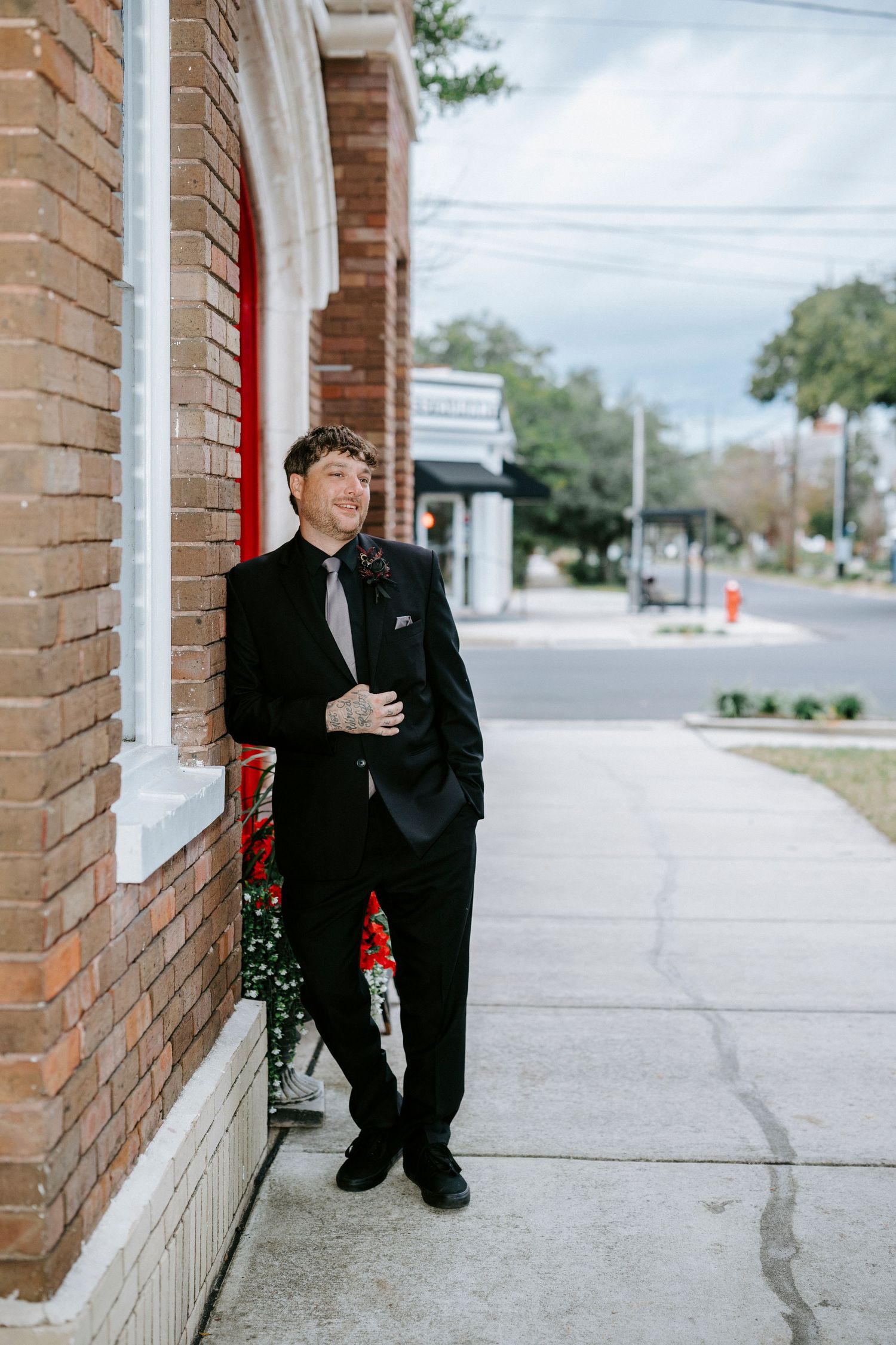A groom in a black suit sits thoughtfully on the steps of a brick building before the ceremony.
